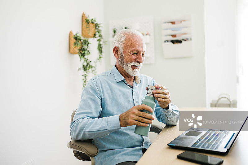 在办公室里从可重复使用的瓶子里喝水的年长男人图片素材