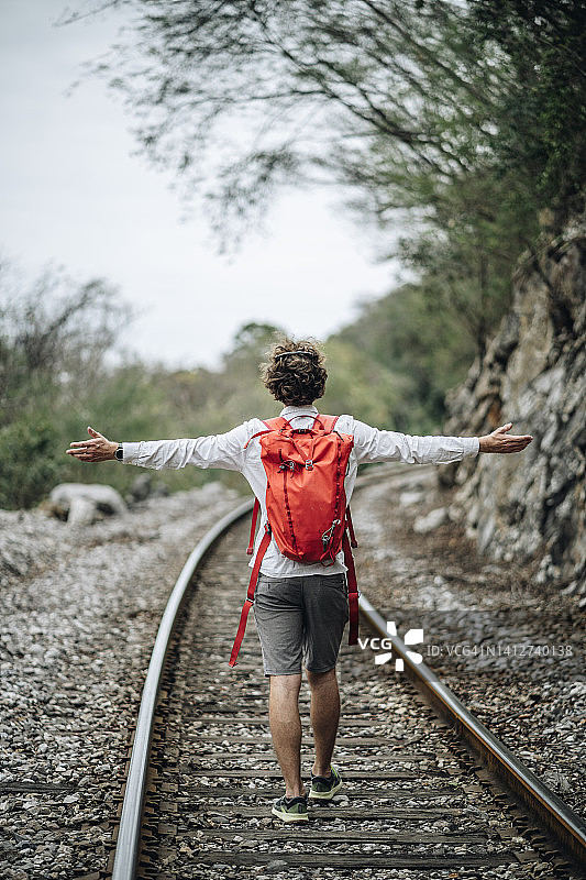 背着背包的年轻男人在丛林中的铁轨上徒步旅行图片素材