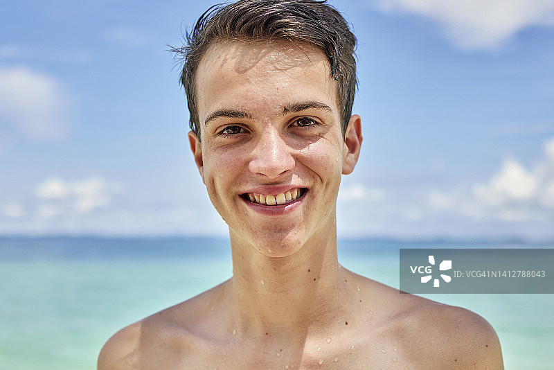 海滩上对着蓝天微笑的少年肖像图片素材