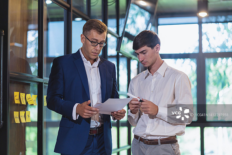 年长的财务战略主管在科技商务办公室与新来的财务人员讨论或交流想法，他们随意地坐在桌旁进行休闲会议讨论图片素材