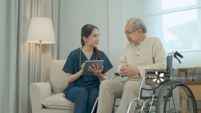 护士和老年病人在家中轮椅上讨论平板电脑图片素材