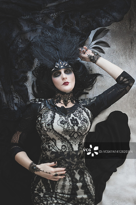 戴羽毛头饰、身穿黑色花纹礼服的优雅女人，灰色背景墙图片素材