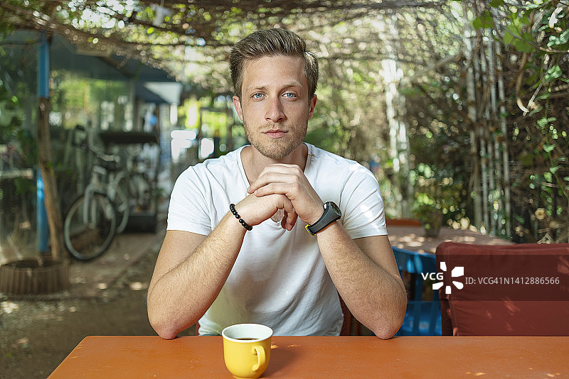 白天坐在咖啡馆外面的桌子旁边的严肃男人肖像图片素材