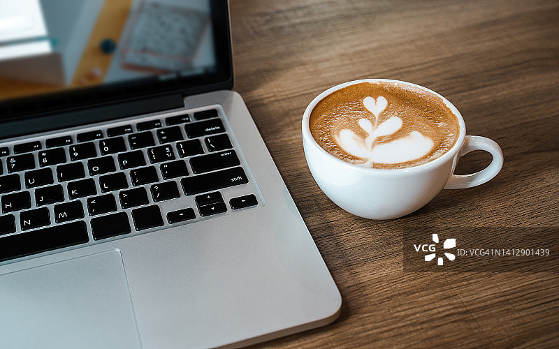 木桌上的笔记本电脑和咖啡杯：咖啡店工作区俯视图图片素材