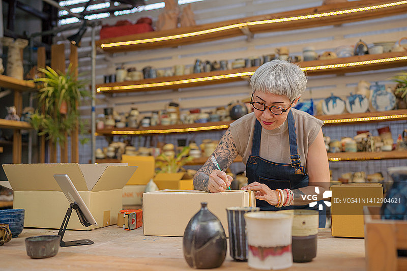 陶器店的女店主正在将产品装在盒子里，并在盒子上书写送货地址图片素材