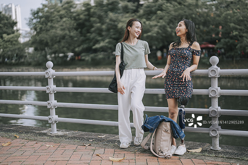 亚洲残疾妇女与朋友在河岸边交谈图片素材
