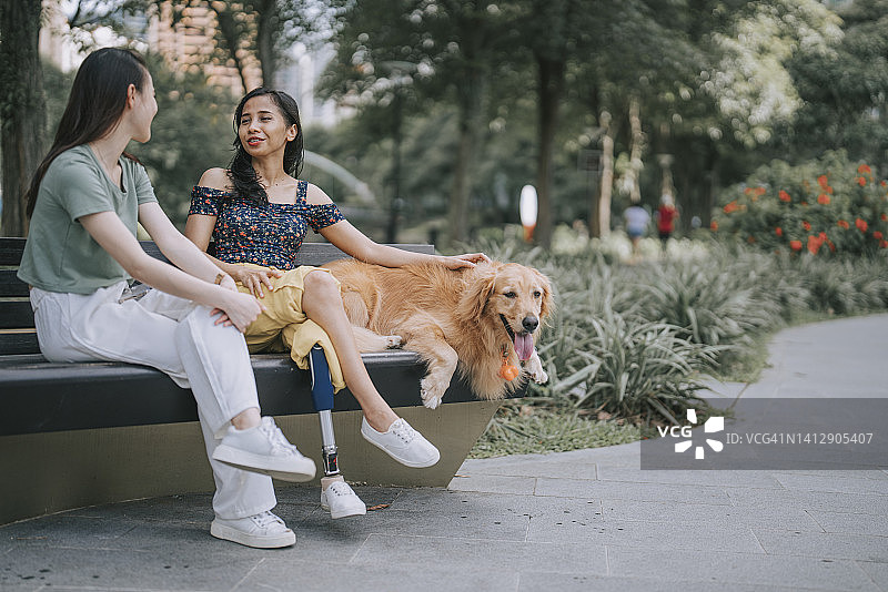 亚洲女人在周末早上与坐在公园长椅上的残疾朋友交谈图片素材