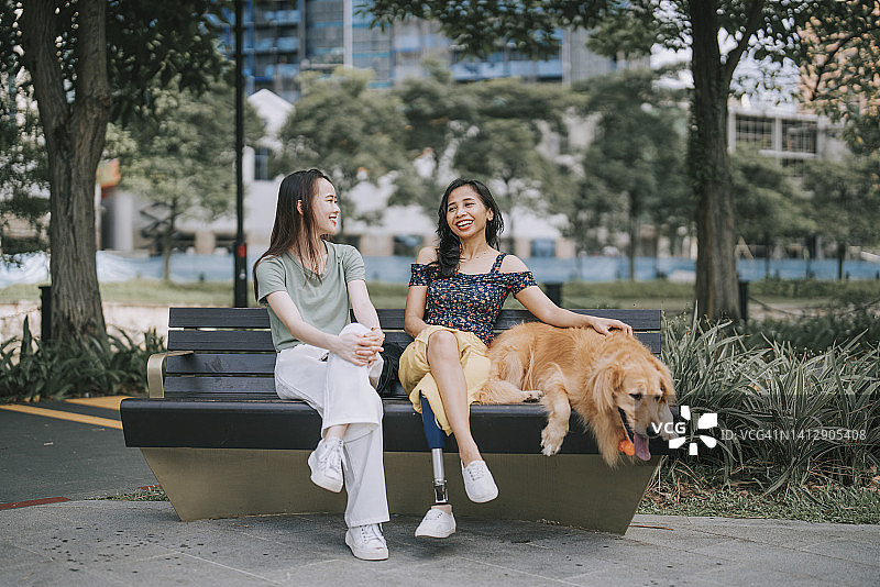 亚洲女人在周末早上与坐在公园长椅上的残疾朋友交谈图片素材