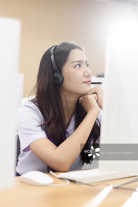 年轻女学生戴着耳机坐在电脑课的桌子旁图片素材