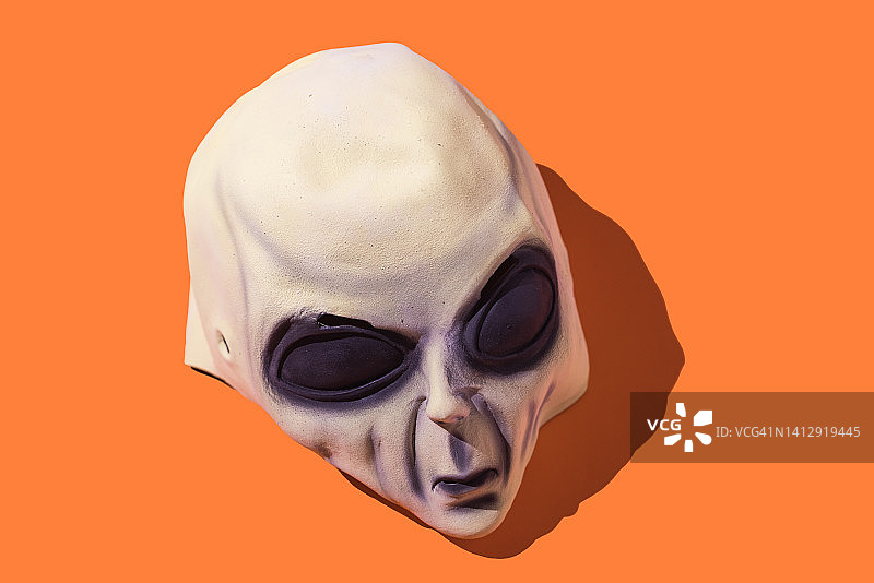 橙色背景上的绿色外星乳胶面具。万圣节庆祝、聚会和伪装概念图片素材