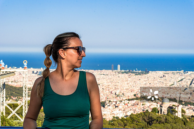 年轻金发女郎在瞭望台上欣赏巴塞罗那壮丽的城市风光图片素材