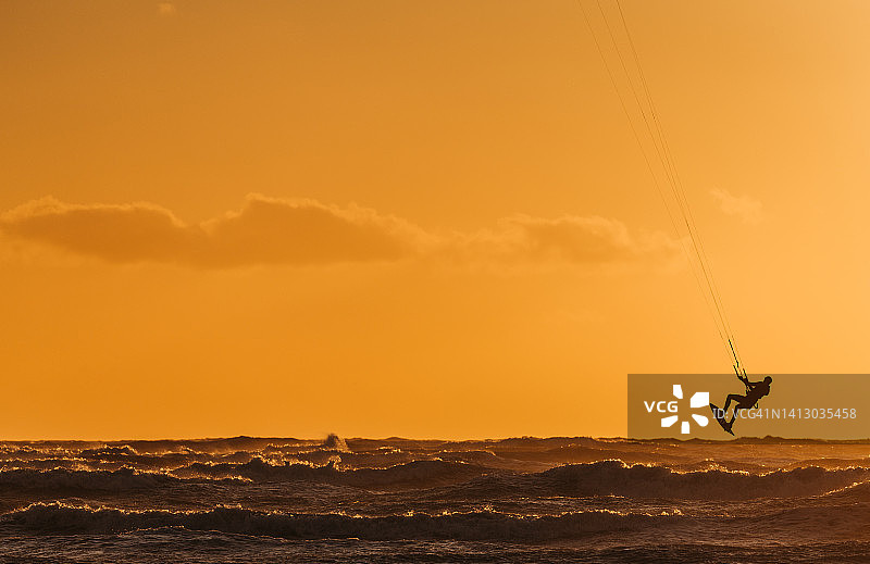 日落时分在波涛汹涌的海面上玩风筝板的人图片素材
