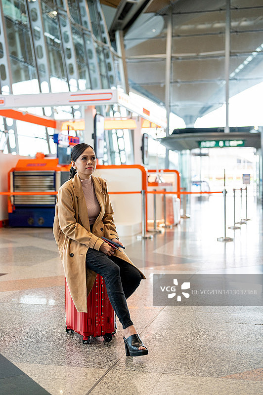 在机场候机区坐在行李上的亚洲女商人图片素材