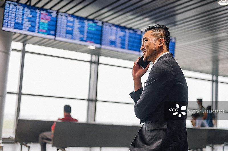 站在出发指示牌前使用手机的亚洲商人：旅行信息互联图片素材