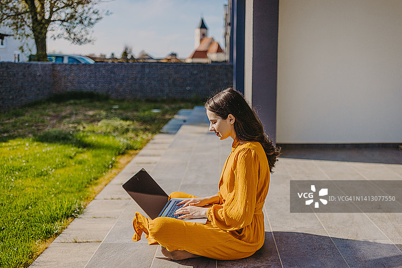 在阳光明媚的日子里坐在门廊上使用笔记本电脑的微笑女人图片素材