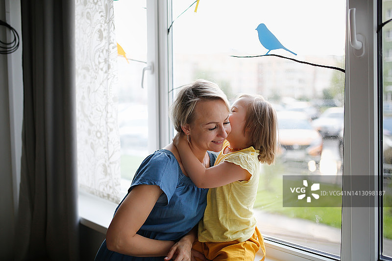 母亲和患有唐氏综合征的女儿在窗边，充满温情图片素材