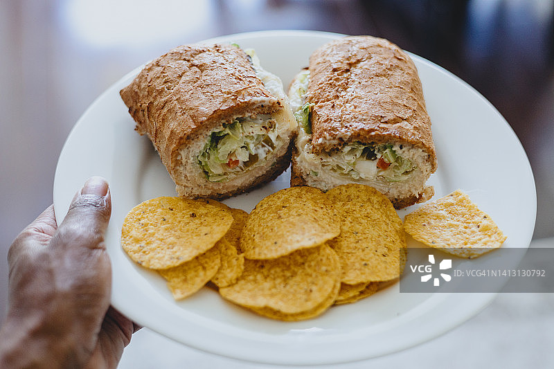 女人拿着一份金枪鱼沙拉三明治和玉米片图片素材