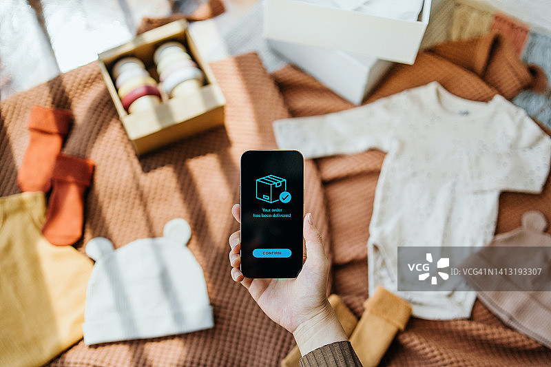 孕妇用手机确认网购的婴儿服装和配饰已送达图片素材