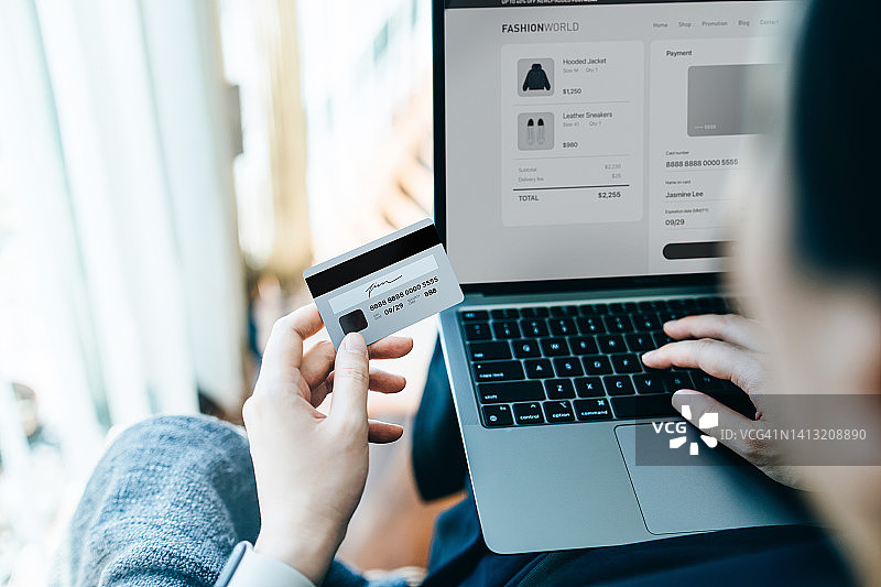 亚洲年轻女子在家放松，在沙发上用笔记本电脑网购并用信用卡在线支付图片素材