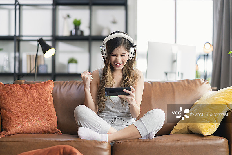 快乐的年轻亚洲女性在沙发上用智能手机玩电竞游戏图片素材