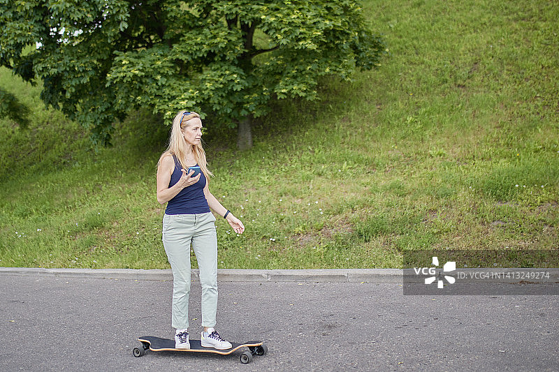 在户外滑板公园长板上的浅色运动服金发苗条年轻女人图片素材