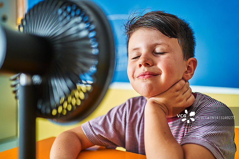 在教室里与电风扇互动的男学生图片素材