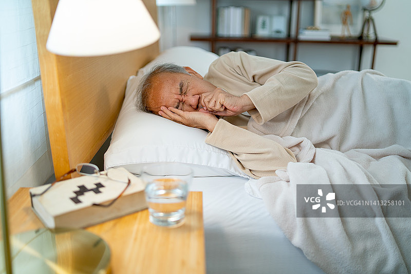 亚洲老年男子独自躺在卧室床上，偶尔咳嗽，继续睡觉，居家养老概念图片素材