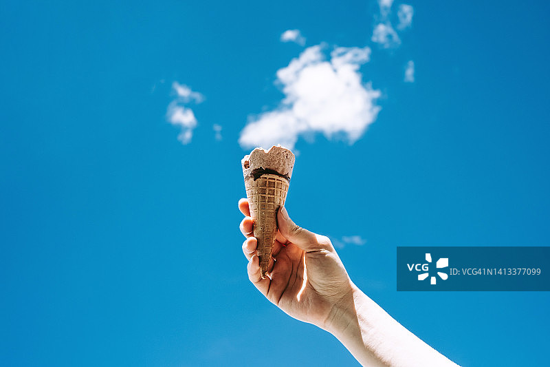 女子手持冰淇淋，背景为蓝色天空图片素材