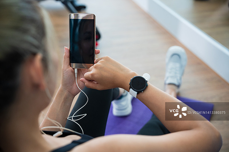 在健身房使用智能手表和手机的年轻女人，通过手机听音乐，运动健康的生活方式图片素材