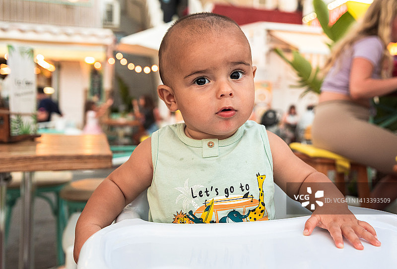 坐在餐厅露台高脚椅上的婴儿的肖像图片素材