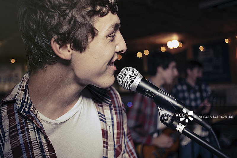 微笑的青少年男孩在车库里对着麦克风唱歌图片素材