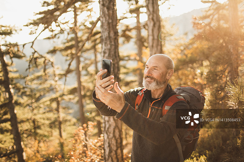 快乐的灰胡子老年男人在森林里散步并自拍，心态年轻图片素材