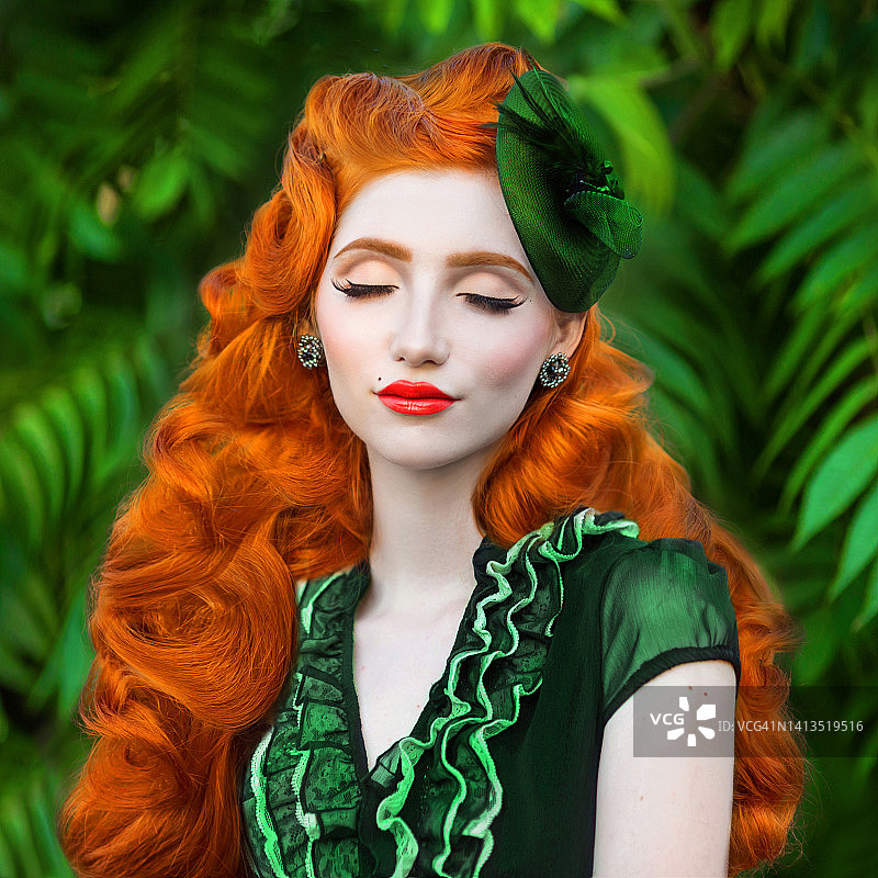 红发美女。长卷发，皮肤白皙。戴帽子，穿绿色连衣裙，以大自然为背景的女孩。红唇美女模特。复古装束。发型。珠宝和装饰品图片素材