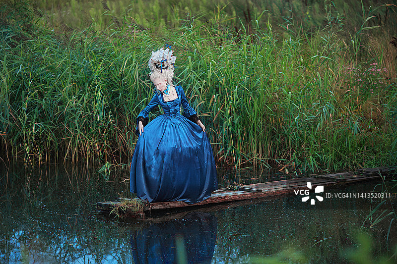 文艺复兴风格的公主，金发，湖面背景。美人妆。童话洛可可女王，发型上有船，自然风光。蓝色连衣裙模特。桥上具有历史发型的女人图片素材