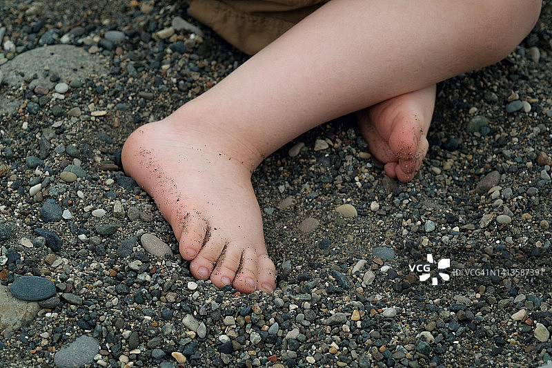 海滩背景下，孩子在蓝色大海边的海卵石上踩着脏脚丫。母子在度假时捡鹅卵石，享受夏季旅游，家庭游客假期的健康积极生活方式图片素材
