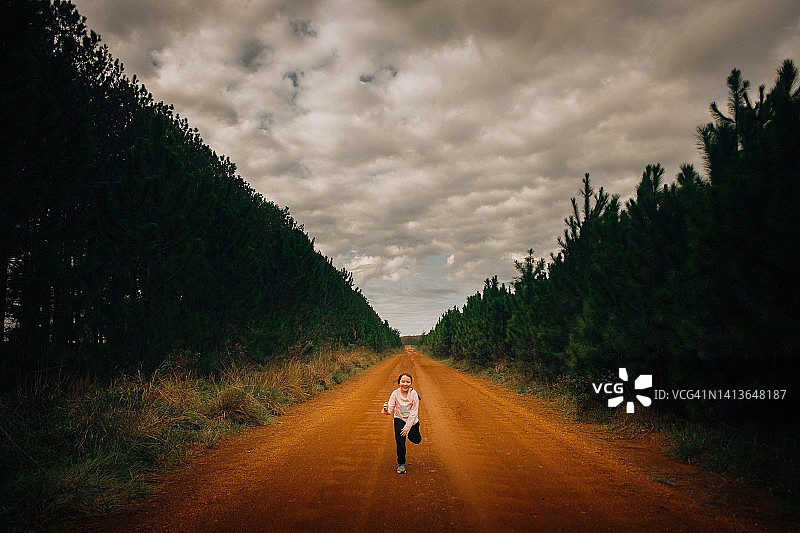 小女孩在红色土路上奔跑，天空乌云密布图片素材