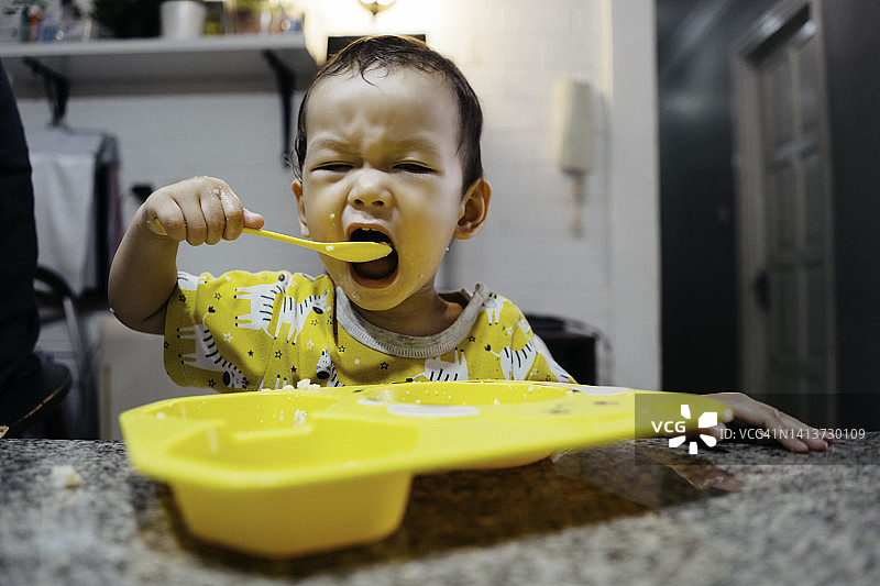 坐在婴儿喂养椅上学习自己吃饭的可爱男宝宝图片素材