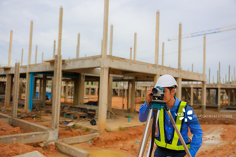 在建筑工地指导戴安全帽和反光背心的测量学徒的亚裔男工程师图片素材