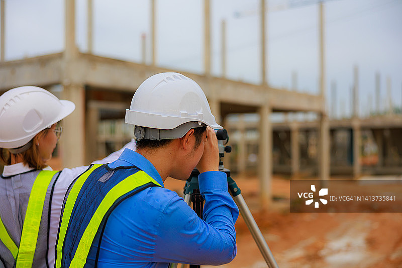 在建筑工地指导戴安全帽和反光背心的测量学徒的亚裔男工程师图片素材