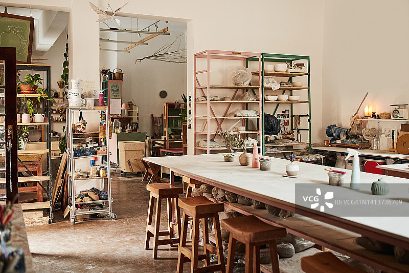 现代陶艺工作室或创意工坊空间内部，摆满了手工艺术品和陶瓷的架子和桌子。黏土模塑和雕塑文化工艺课程，配有木椅。图片素材