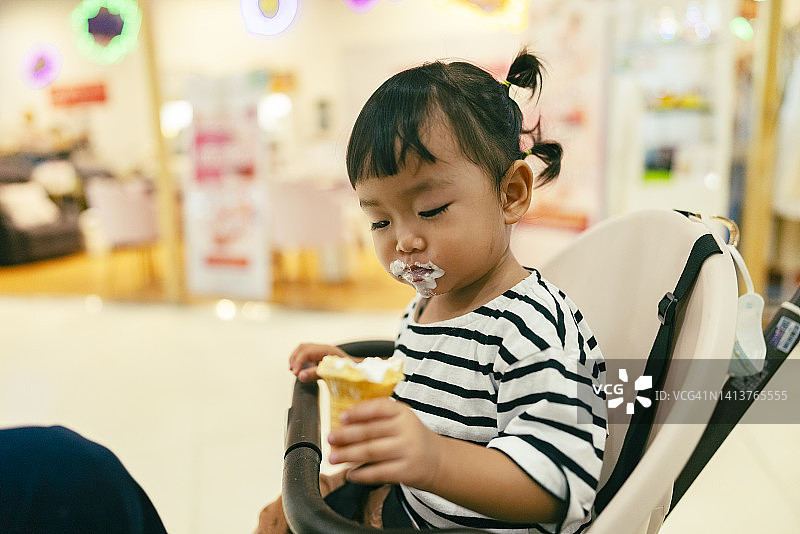 亚裔女婴第一次吃冰淇淋，嘴上沾满奶油，非常高兴图片素材