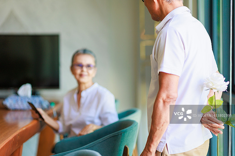 一位亚洲老年男子在家中给妻子送上一束玫瑰花。图片素材