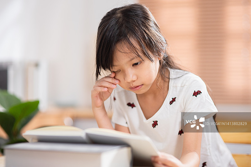 亚洲女学生试图专注于阅读书籍，以缓解在家在线学习时的近视图片素材