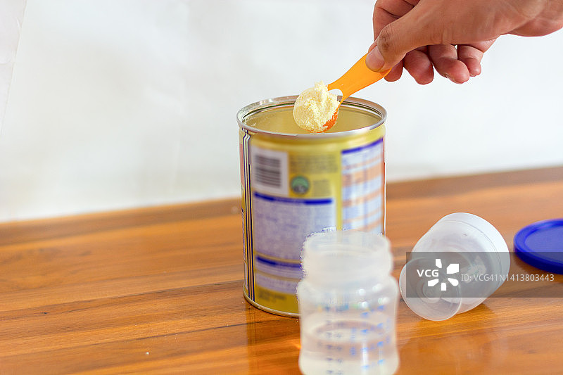 特写：浅色背景下的奶粉和蓝色勺子。罐中量勺里的婴儿奶粉，以及婴儿奶粉和奶瓶。图片素材