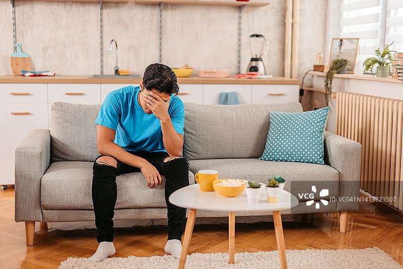 坐在家里，看起来悲伤和心烦意乱的年轻男人图片素材