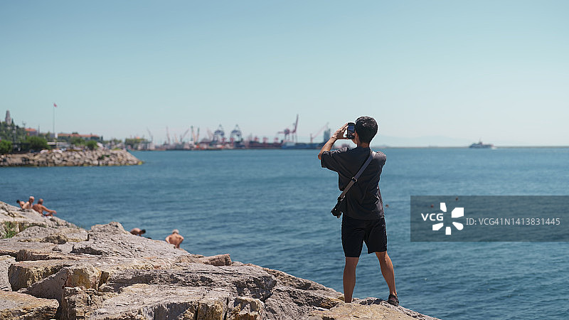 在海边用手机拍照录像的年轻男游客图片素材