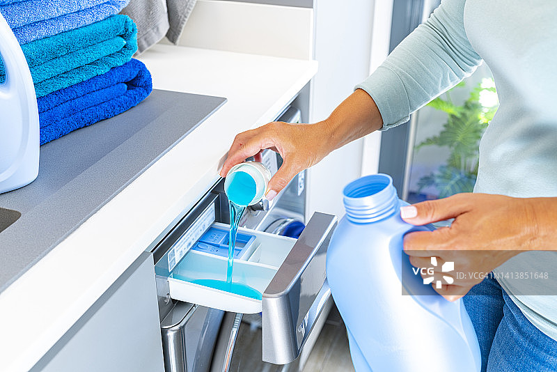 女人向洗衣机中加入衣物柔顺剂或洗涤剂图片素材