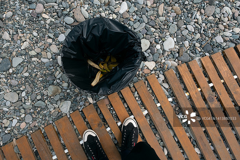 海边垃圾桶上的塑料袋。一名男子或学生将香蕉皮扔进大自然中的垃圾桶。清洁海滩，维护秩序。环保，环境保护。旅游、休闲、旅行概念。留白图片素材