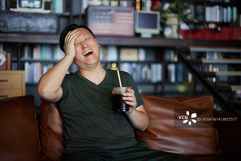 男人坐在沙发上看电视，开怀大笑图片素材