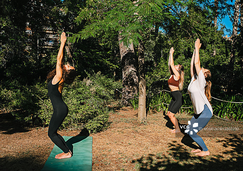 三位年轻女性在田野里做椅子瑜伽，在草地上做 Utkatasana 的运动女孩图片素材
